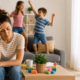 Madre stanca mentre due bambini giocano in casa durante l’estate, immagine sulle difficoltà dei genitori nella gestione dei figli.